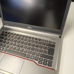 Fujitsu laptop on a light surface, screen off, silver body with a red-edged keyboard area visible.